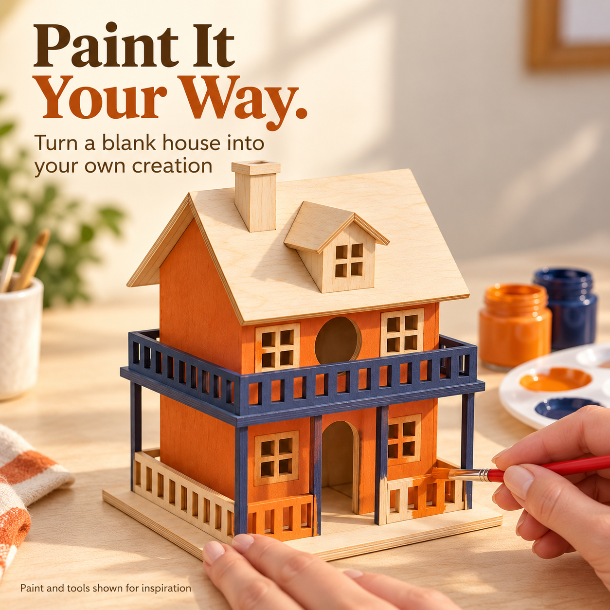 Hands painting the porch of a miniature wooden house orange